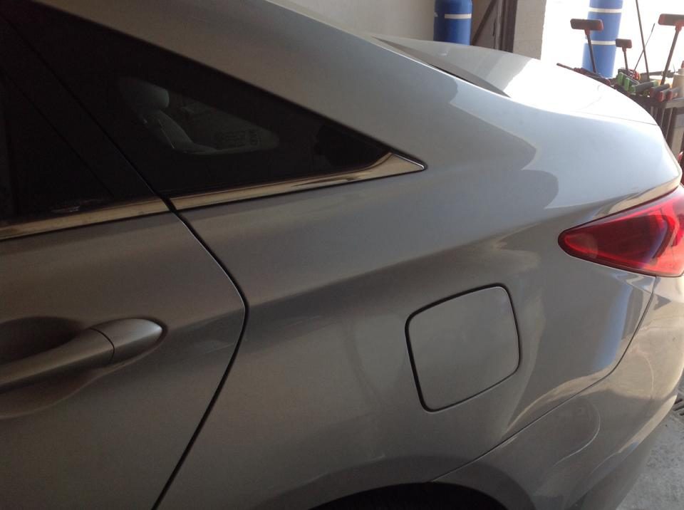 A dent in the rear body panel of a silver SUV before paintless repair